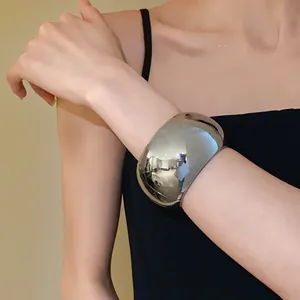 Detail view of a chunky silver polished wide cuff bracelet worn on the wrist.