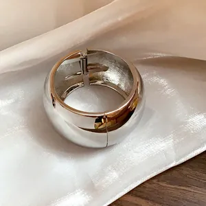 Detailed close-up view of a wide polished silver metallic bangle with hinged opening mechanism