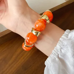 Dettaglio di un bracciale in acrilico marmorizzato arancione con distanziatori in metallo oro