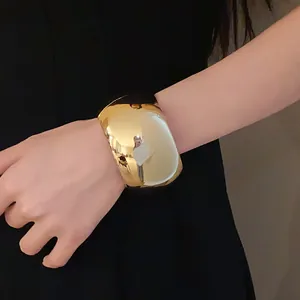 Close-up of wide glossy gold metal cuff bracelet on wrist showing reflective surface