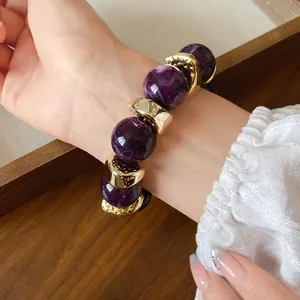 Dettaglio di un bracciale in acrilico marmorizzato viola con accenti dorati sul polso
