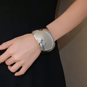 Close-up view of a large polished silver metallic open cuff bracelet worn on the wrist