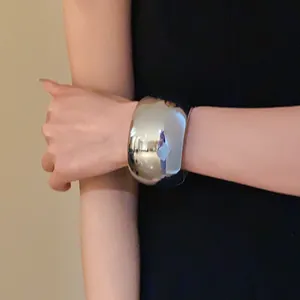 Detailed close-up view of a wide polished silver metallic cuff bracelet worn on a wrist