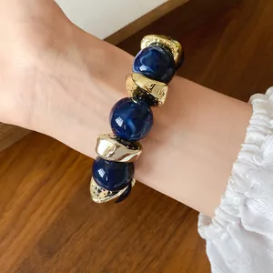 Primo piano di perline in acrilico blu marmorizzato e distanziali dorati su bracciale