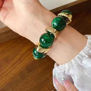 Primo piano di un braccialetto di perle acriliche verdi marmorizzate con inserti dorati.