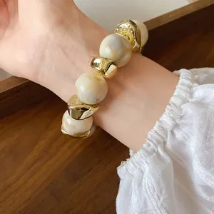 Primo piano di un elegante bracciale in perle di acrilico marmorizzato con finiture oro.