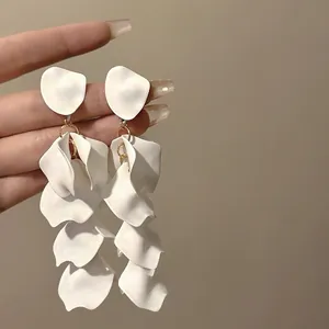 Close-up detailed view of elegant white matte petal tassel earrings held by a hand.