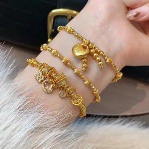 Close-up of gold-plated bracelets featuring a traditional luck charm and crystal accents