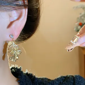 Detailed close-up of gold pleated leaf earrings with a crystal stud on a model's ear