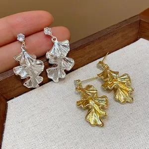 Close-up of ruffled leaf earrings in gold and silver finish with crystal studs