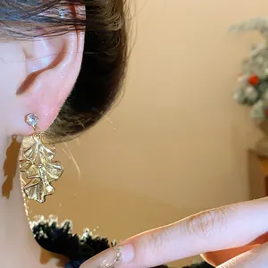Macro detail of elegant gold wrinkled leaf earring with crystal stud worn on ear