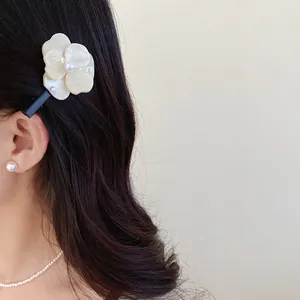 Close-up of a sweet white flower hair clip with pearl detail worn in black wavy hair.