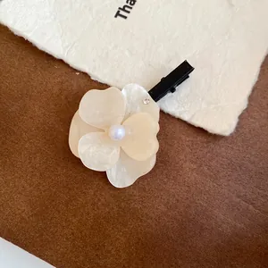 Close-up of elegant white acrylic flower hair clip with pearl center and rhinestone detail.