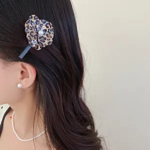 Close-up of a stylish leopard print flower hair clip with pearl center on model's hair