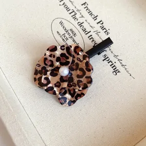 Aesthetic leopard print flower hair clip with a central pearl on a vintage beige box.