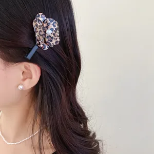 Close-up detail of a leopard print flower hair clip with pearl worn on elegant dark hair