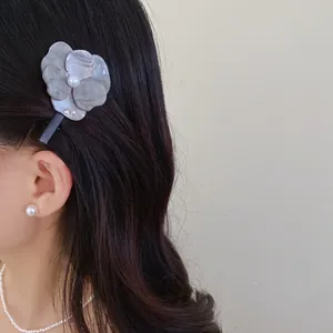 Elegant grey flower hair clip with a central pearl shown on a dark hair model