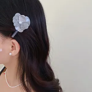 Close-up of elegant flower hair clip with pearl center worn on dark wavy hair