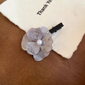 Close-up of a marble-textured flower hair clip with a pearl center on a white card.