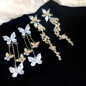 Macro detail showing crystal butterfly and floral long drop earrings on black fabric.