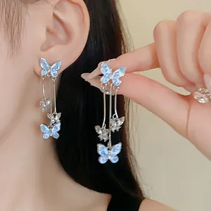 Close-up detail of delicate light blue crystal butterfly long drop earrings worn by model