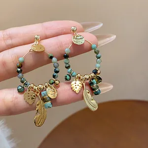 Dettaglio ravvicinato di orecchini a cerchio boho placcati oro con perline e piume retrò