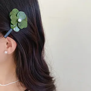 Close-up of elegant green flower hair clip with pearl detail worn on hair