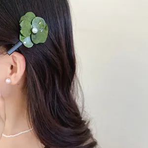 Close-up of a stylish green floral duckbill hair clip with pearl detail on dark hair