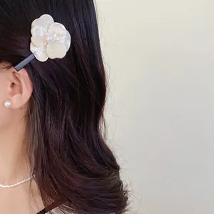 Elegant cream flower hair clip with pearl detail worn on long wavy brown hair.