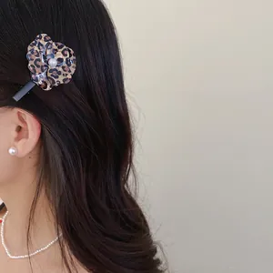 Elegant leopard print flower hair clip with pearl center worn on wavy brown hair