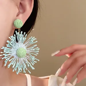 Close-up of handmade woven flower earrings in light green and white.