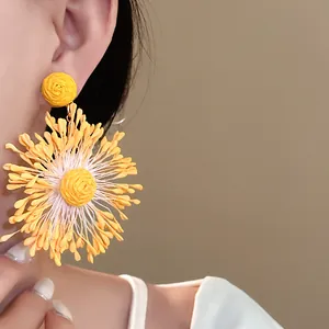 Close-up detail of handmade woven yellow flower earrings featuring firework petal design