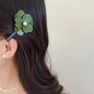 Close-up detail shot of a green resin flower hair clip with a pearl center on dark wavy hair.