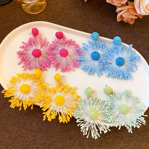 Macro detail of colorful handmade woven flower earrings in pink, blue, and yellow.