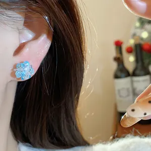 Detailed view of sparkling blue and clear crystal flower stud earrings worn on model ear