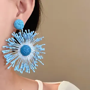 Detailed close-up view of blue handmade woven flower earrings on a model's ear