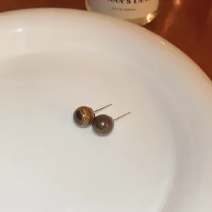 Macro view of vintage tiger eye stone stud earrings displayed on a white ceramic plate