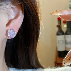 Close-up of a lavender crystal flower stud earring worn on the earlobe with warm lighting.