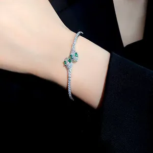 Vista detallada de una elegante pulsera de serpiente plateada con piedras verdes.