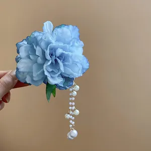 Macro detail of an elegant blue fabric flower hair clip featuring a dangling pearl tassel