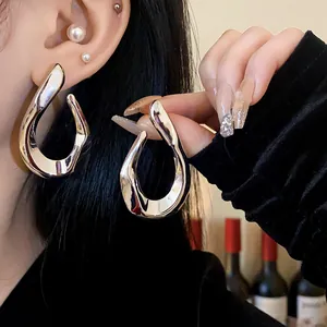 Close-up detail of oversized silver twisted metal hoop earrings with a shiny finish.