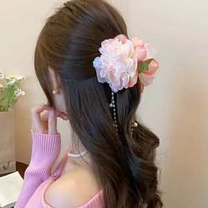 Detail of a pink fabric flower hair clip with elegant pearl tassels on long brown hair