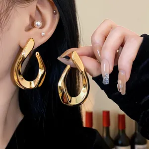 Detail view of a glossy gold twisted metal hoop earring worn by a model.
