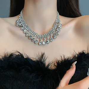 Detailed view of a silver rhinestone statement necklace with square crystal drops on model.