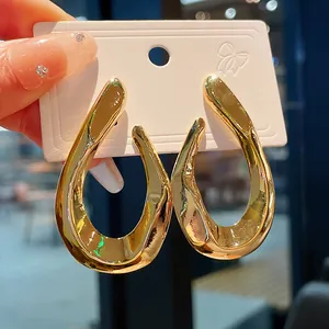 Close-up view of oversized twisted gold metal hoop earrings with a glossy finish.