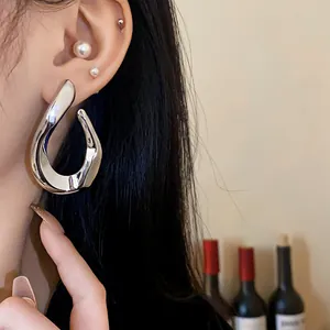 Close-up of exaggerated twisted silver metal hoop earrings worn by a fashion model