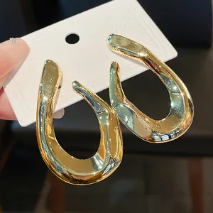 Close-up detail of distorted gold-toned metal hoop earrings with high-gloss finish.