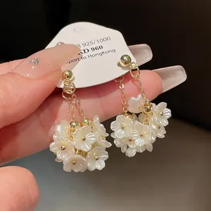 Gros plan de boucles d'oreilles pompons dorées avec de délicats bouquets de fleurs blanches.
