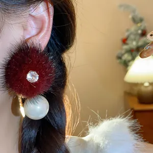 Primo piano di orecchini a pompon in pelliccia bordeaux con zircone e goccia di perla