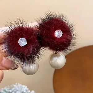 Primo piano di eleganti orecchini a pompon bordeaux con zirconi e dettagli in perle.